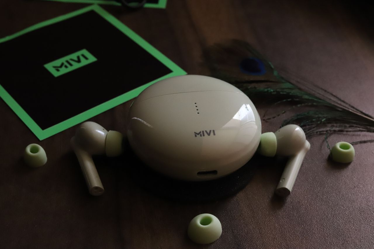 services-02 Wireless earphones with a sleek charging case placed on a wooden table alongside ear tips and a feather.