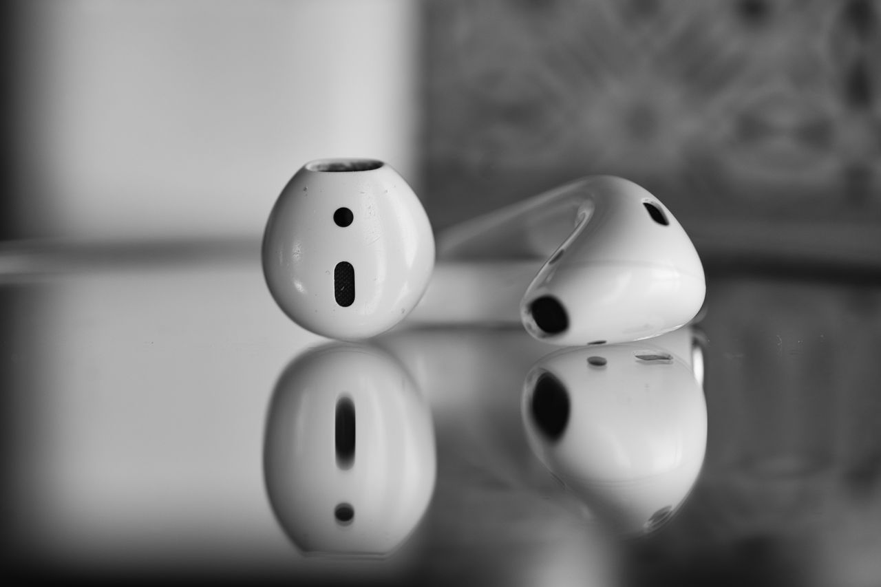 services-04 Close-up of wireless earbuds with reflection in black and white.